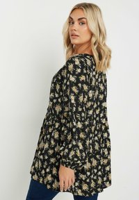 Svart blommig blus med peplumdesign, långa ärmar och en mjuk textur med små pastellblommönster överallt.