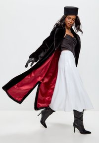 Zwarte faux fur jas met rode voering, getailleerde zwarte korset top, vloeiende witte met pailletten bezaaide rok, en zwarte stiletto boots.