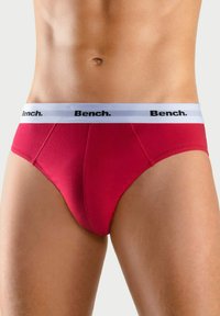 Rode stofen slip met witte elastische tailleband waarop het "Bench." logo in het zwart staat. De gladde textuur en de getailleerde pasvorm accentueren de lichaamsvorm.