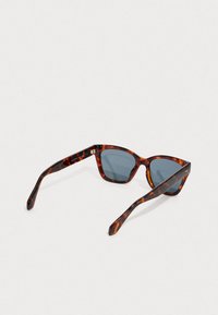 Obdélníkové sluneční brýle s želvovinovým vzorem a tmavě modrými skly ležící na bílé ploše s jedním rámem vytaženým.