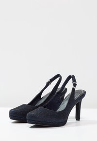 Zapatos de tacón abiertos de color azul marino con una textura brillante, punta afilada y un tacón alto y delgado. Cuentan con una hebilla ajustable y plantilla acolchada.