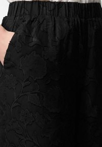 Mustad lillemustriga püksid elastse vöörihma ja küljetaskutega, millel on tekstuurse kangaga õrn läige.