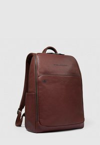 Bruine leren rugzak met een gestructureerd ontwerp, voorzien van een voorvak met rits, een handvat aan de bovenkant en gewatteerde schouderbanden.