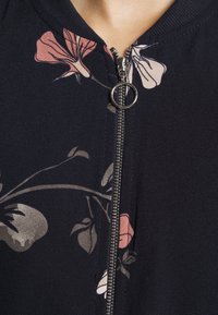 Maritiem, rits vest met bloemmotieven in lichtroze en beige. Getextureerde stof met een ronde halslijn en metalen ritsdetail.