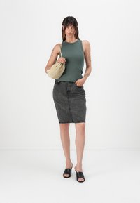 Grønn ribbet singlet, høy midje svart denimskjørt, svarte slip-on sko og beige skulderveske; viser en urban avslappet stil.