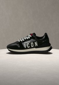 Baskets noires avec semelle blanche et lacets, avec le texte "DSQUARED2 ICON" sur le côté, exposées sur une surface claire avec un fond neutre.