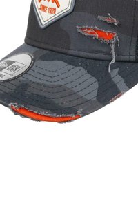 Black camouflage cap with a distressed brim, orange accent stitching, and an embroidered logo patch. Features frayed edges and textured fabric.