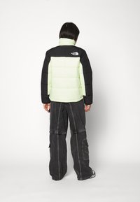 Nafukovací bunda s čiernou hornou časťou a svetlozelenou dolnou časťou. Má vysoký golier a logo The North Face na zadnej strane.