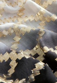 Tissu tissé présentant un motif en zigzag en or métallique et en nuances de gris, mettant en valeur une texture lisse et des détails complexes.