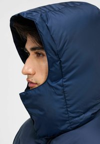Granatowa kurtka puchowa z kontrastującym kapturem i wysokim kołnierzem. Gładki, błyszczący materiał z pikowaną fakturą. Posiada zamek błyskawiczny z przodu.