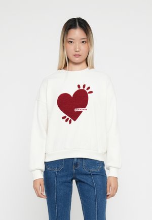 Felpa bianca con un design a cuore rosso testurizzato e la scritta "Coup de Coeur." Presenta maniche lunghe e una silhouette morbida.