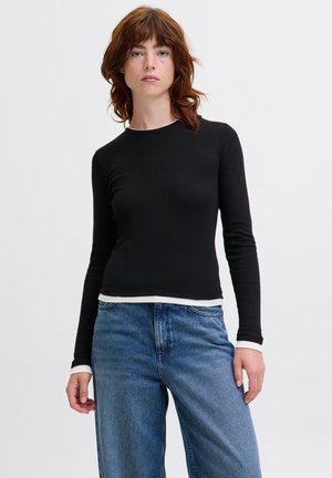 Schwarzes Langarmshirt mit rundem Halsausschnitt, ausgestattet mit weißen Akzenten an den Ärmeln und dem Saum. Kombiniert mit hoch taillierten blauen Jeans.