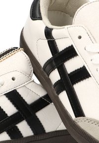 Zapatillas de cuero blancas con rayas horizontales negras, suela texturizada y detalles en negro contrastantes en el talón y la lengüeta.