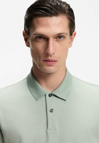 Hellgrünes Polohemd mit strukturierter Stoffqualität, kurzen Ärmeln und Kragen. Verfügt über drei Knöpfe und ein klassisches Design.