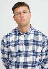 Camicia con bottoni caratterizzata da un motivo a quadri blu e bianchi, realizzata in tessuto morbido con colletto e bottoni frontali.