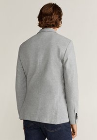 Blazer grigio realizzato in materiale morbido, caratterizzato da una vestibilità sartoriale, rever con intaglio e polsini con bottoni. Cuciture visibili e texture liscia.
