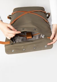 Olivgrüner Rucksack mit Lederakzenten, ausgestattet mit einem oberen Klappdeckel, Druckknopfverschluss und einem gefütterten Innenraum mit einer Tasche und einem Riemen zur Organisation.