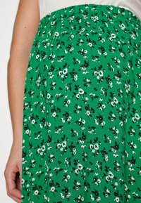 Jupe verte à motif floral avec une taille élastique. Présente des fleurs blanches et noires sur un tissu vert vif. Texture légère.