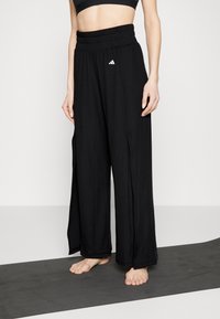 Schwarze Hosen mit weitem Bein aus leichtem Stoff, mit hohem elastischem Bund und kleinem weißem Logo auf der Vorderseite.