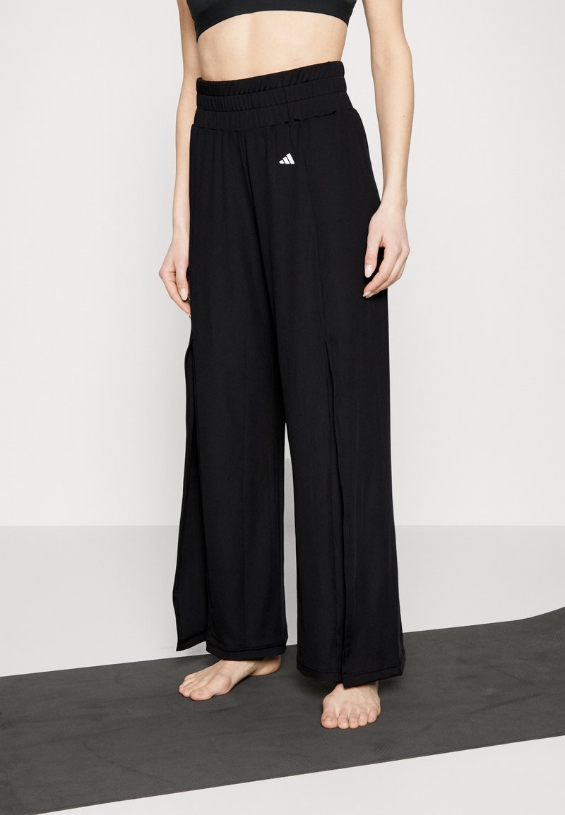 Schwarze Hosen mit weitem Bein aus leichtem Stoff, mit hohem elastischem Bund und kleinem weißem Logo auf der Vorderseite.