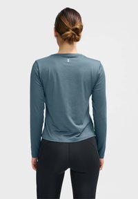 Lange mouw sporttop in lichtblauwe stof, met een subtiel patroon, voorzien van een ronde halslijn en een klein logo op de achterkant.
