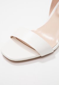 Bílé kožené nazouváky s širokým popruhem a plochou čtvercovou špičkou, hladkým povrchem a minimalisticým stylem.