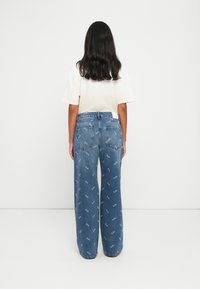 Vaaleansiniset leveälahkeiset farkut, joissa on brodeerattuja kuvioita. Korkea vyötärö ja takataskut; yhdistetty kermaiseen puseroon.