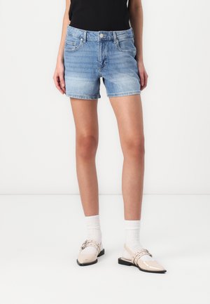 Shorts de mezclilla en azul claro, con una cintura clásica, bolsillos frontales y un dobladillo ligeramente deshilachado. Combinados con calcetines blancos y zapatos beige.