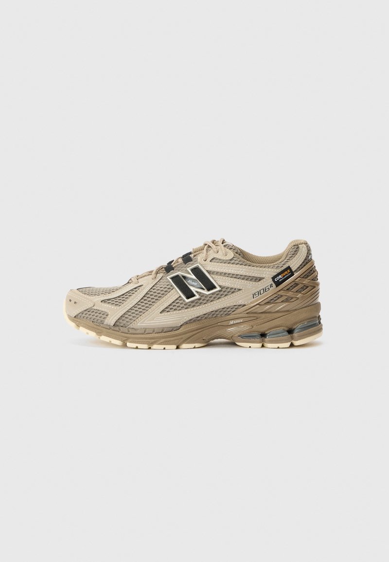 Chaussure de course New Balance 1906R beige et marron avec tige en mesh, fermeture à lacets et semelle rembourrée, présentée de profil sur fond blanc.