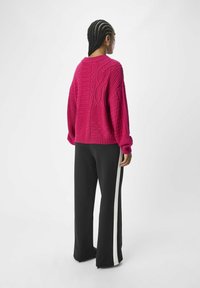 Fuchsia chunky gebreide trui met textuurpatronen, gecombineerd met zwarte wijd-uitlopende broek met een witte zijstreep.