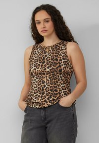 Weste mit Leopardenmuster in Braun- und Schwarztönen, aus weichem Stoff mit lockerer Passform. Kombiniert mit dunkelgrauen Jeans.