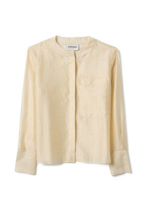 Blusa a maniche lunghe color crema con colletto rotondo, tasca frontale a sinistra, bottoni nascosti e polsini ampi.