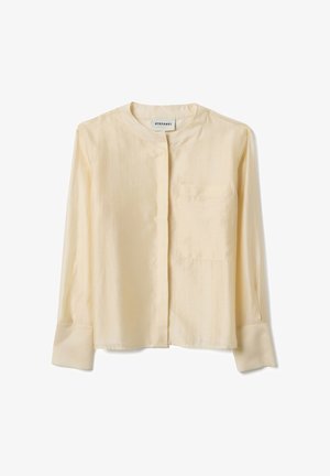 Roomkleurige blouse met lange mouwen, ronde kraag, voorzak aan de linkerzijde, verborgen knopen en brede manchetten.