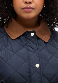 Μπουφάν σε ναυτικό μ πλε με επένδυση, διαθέτει καφέ γιακά από κοτλέ, κλείσιμο με ασημί κουμπιά και σχέδιο διαμαντιών σε όλο το ύφασμα.