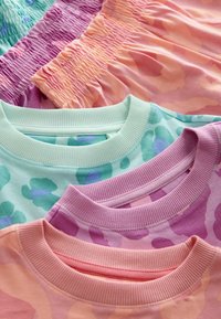 Tre t-shirt color pastello con collo a costine, caratterizzate da motivi astratti nelle tonalità di verde, viola e pesco, sovrapposte a morbidi pantaloni corti testurizzati.