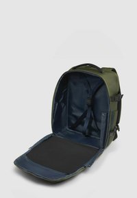 Groene rugzak met een ruim, open interieur. Heeft een blauwe voering, verstelbare riemen en een zwart bodemvlak. Ritsopening toegankelijk.