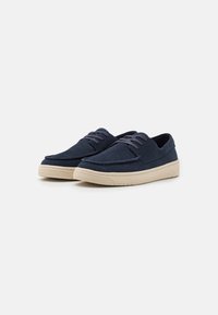 Zapatos de ante azul marino con suelas de goma beige, puntera redondeada, detalles de costura y diseño de cordones a juego. Textura suave con acentos mínimos.