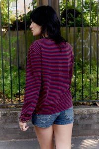 Cămașă cu mânecă lungă cu dungi roșii și albastre, combinată cu pantaloni scurți din denim. Cămașa are un croi lejer și textură în relief.