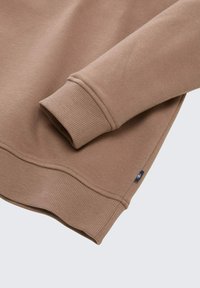 Bruine sweatshirt in de hoek met een geribbelde boord en zoom, een zachte textuur en een klein merklabel aan de zijkant.