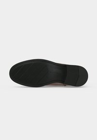 Semelle de chaussure de ville noire avec des zones de grip texturées au talon et à l’avant, présentée sur un fond clair uni.