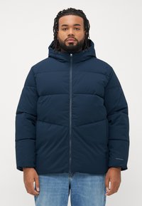 Navy blue puffer jacket with a hood, featuring a zip closure, horizontal stitching, and a subtle logo on the sleeve. Made from insulated fabric.