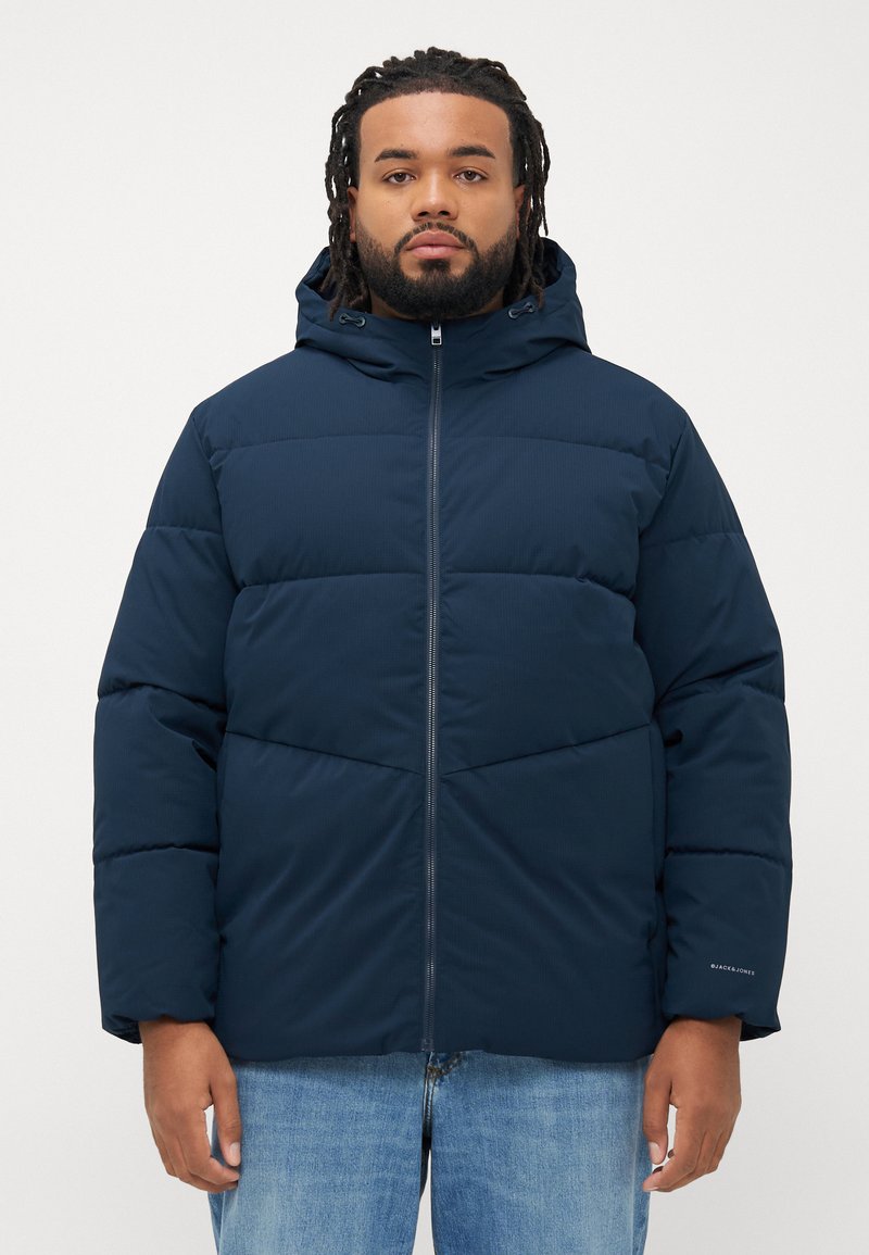 Navy blue puffer jacket with a hood, featuring a zip closure, horizontal stitching, and a subtle logo on the sleeve. Made from insulated fabric.