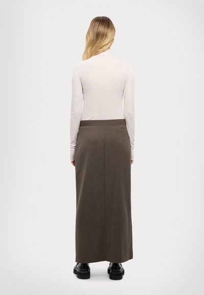 Hosszú, barna szoknya, amely textúrált szövetből készült és egyenes szabású. Egy fitted világos felsővel és masszív fekete cipőkkel párosítva.