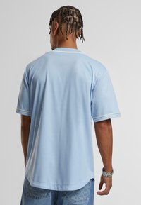 Maglia azzurro chiaro con maniche corte, rifiniture bianche sui polsini e vestibilità ampia. Presenta un collo rotondo e un tessuto morbido e strutturato.