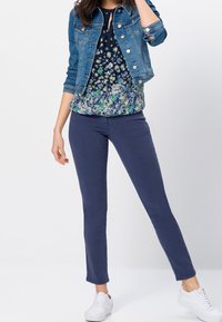 Džínová bunda v tmavě modré barvě se stříbrnými knoflíky, květinová námořnická blouse a úzké námořnické kalhoty. Bílé tenisky dotvářejí vzhled.