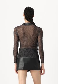 Crna mrežasta majica dugih rukava s uzorkom leopard printa, uskog kroja, visokog vrata i glatke teksture; u kombinaciji s crnom kožnom mini suknjom.