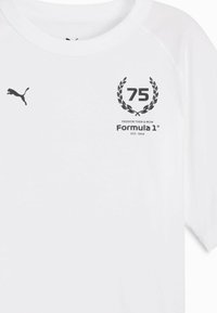 Biała koszulka z czarnym logo Puma, okrągłym emblematem 75 z laurowym wieńcem oraz napisem "Formula 1" poniżej. Miękki materiał, okrągły dekolt.