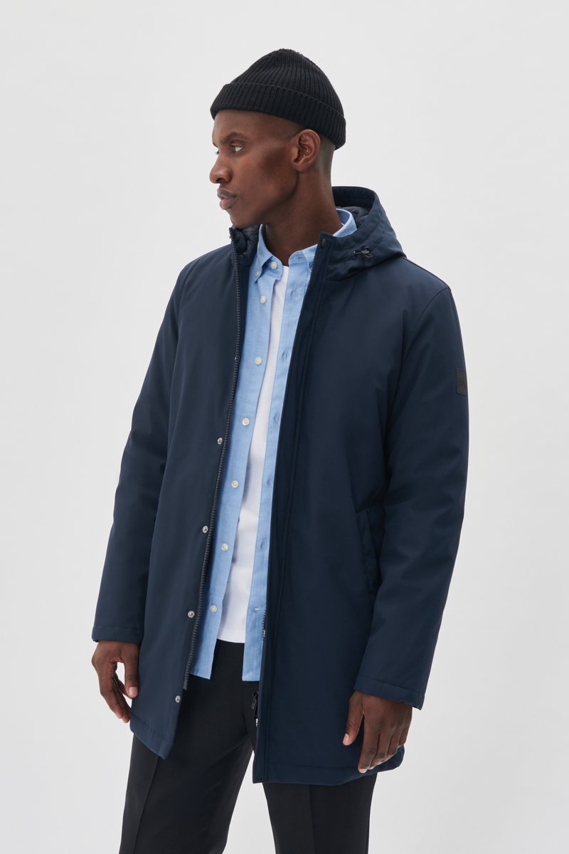 Parka en azul marino con capucha, cremallera delantera y cierre de botón. Presenta una textura suave y detalles de hardware en negro.