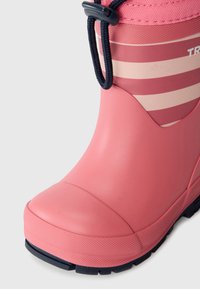 Primer plano de una bota de goma rosa con una suela texturizada y cordones azul oscuro, que presenta rayas horizontales en tonos más claros de rosa.