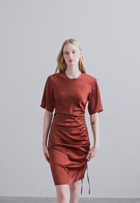 Rochie din satin de culoare ruginită, cu mâneci scurte, detalii frunză pe lateral și legături ajustabile la tiv, având o textură netedă.